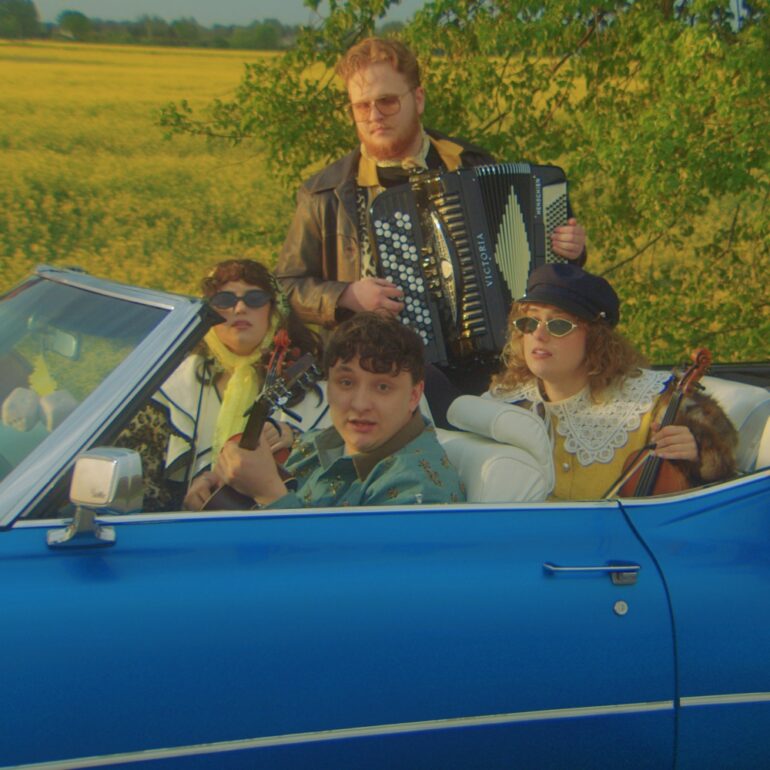 Group of four retro-styled musicians in a bright blue vintage car: driver in teal shirt, front passenger with a guitar, and two women in the backseat (one with sunglasses and lace collar, the other holding a violin); a man stands behind them playing an accordion.