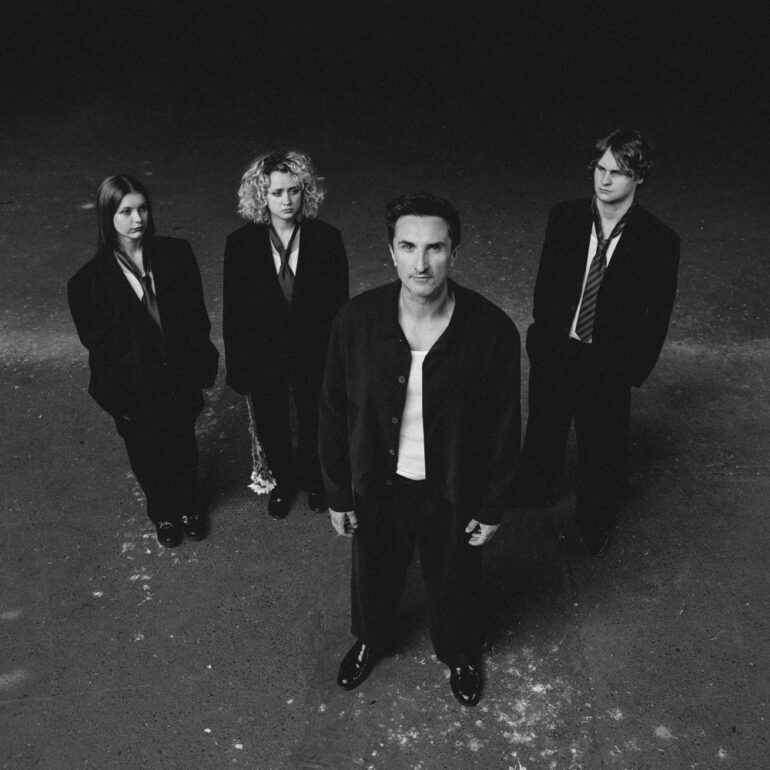 Black-and-white group portrait of a four-person band standing on a concrete surface, facing the camera.