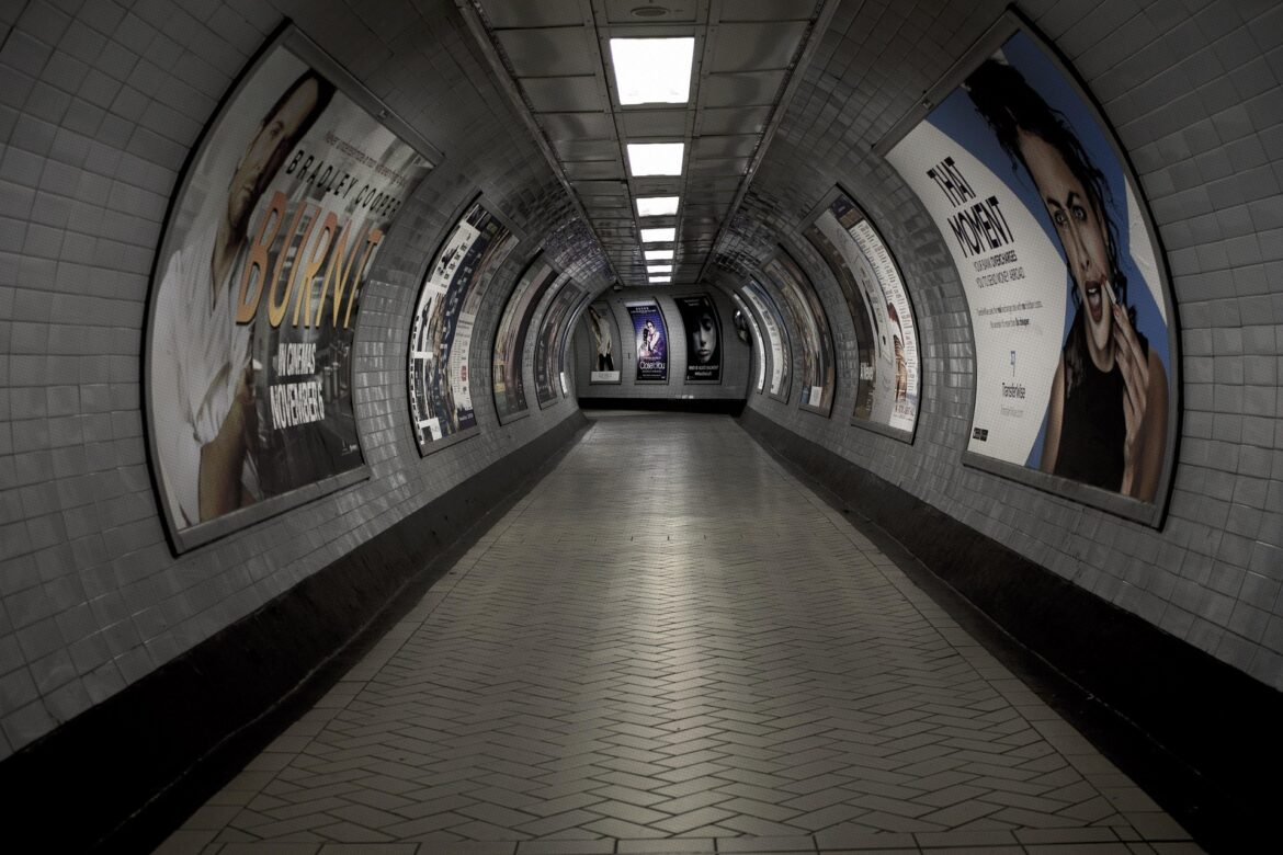 Curved underground subway passage lined with posters on tiled walls, perspective toward the far end.