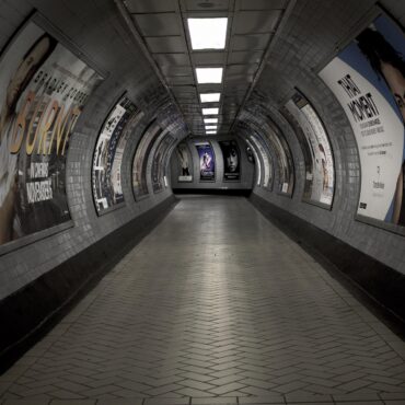 Curved underground subway passage lined with posters on tiled walls, perspective toward the far end.