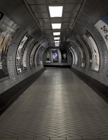 Curved underground subway passage lined with posters on tiled walls, perspective toward the far end.