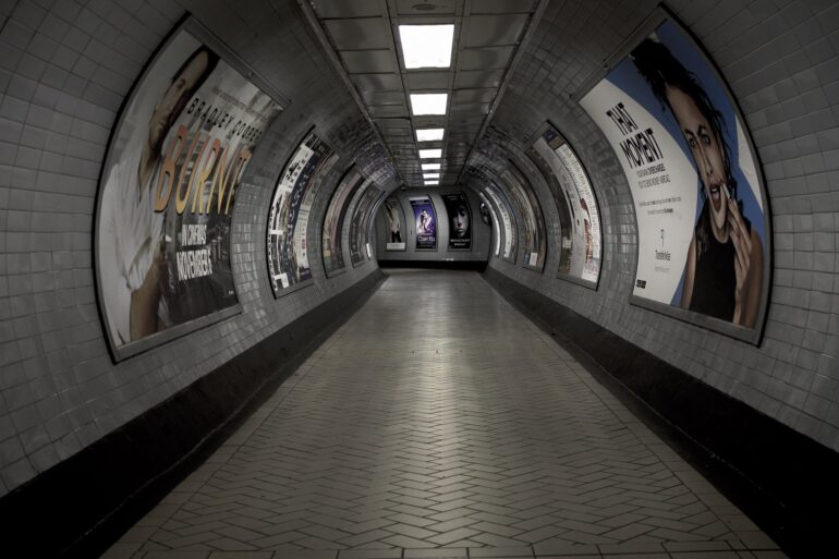 Curved underground subway passage lined with posters on tiled walls, perspective toward the far end.