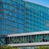 Glass-front modern office building with blue-tinted windows and metal framing, under a clear sky
