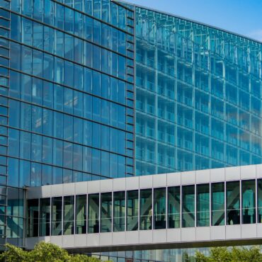 Glass-front modern office building with blue-tinted windows and metal framing, under a clear sky