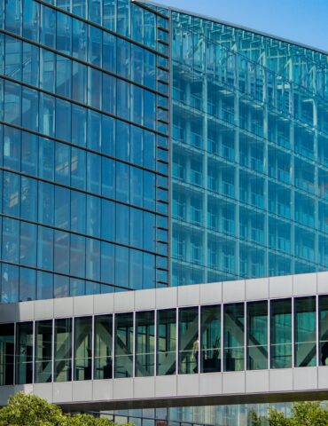 Glass-front modern office building with blue-tinted windows and metal framing, under a clear sky
