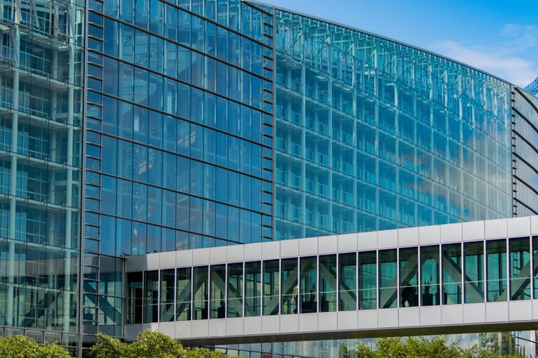 Glass-front modern office building with blue-tinted windows and metal framing, under a clear sky