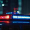 Police car roof with red and blue emergency lights flashing at night in a city setting.