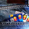 Back pocket of blue denim jeans with several Mastercard credit cards peeking out, orange stitching visible along the pocket edge.