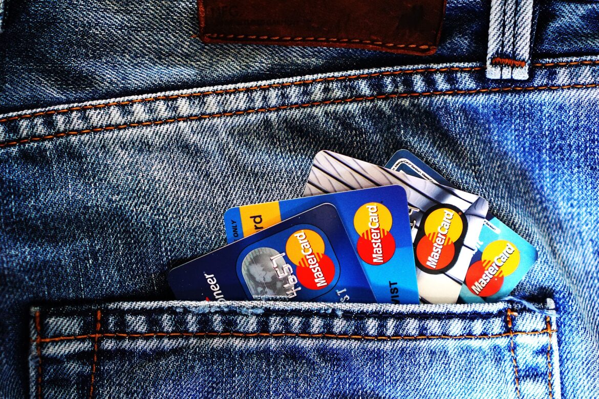 Back pocket of blue denim jeans with several Mastercard credit cards peeking out, orange stitching visible along the pocket edge.