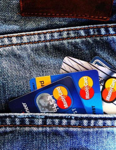 Back pocket of blue denim jeans with several Mastercard credit cards peeking out, orange stitching visible along the pocket edge.