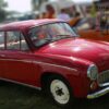 Red vintage car shown from the side and front at a car show, with whitewall tires and chrome trim on a grassy field.