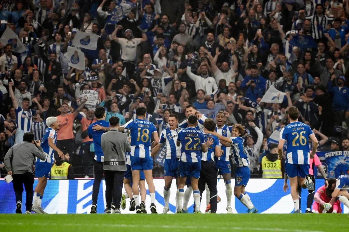 Soccer players in blue-and-white uniforms celebrate a goal on the field with cheering fans in the stands behind them