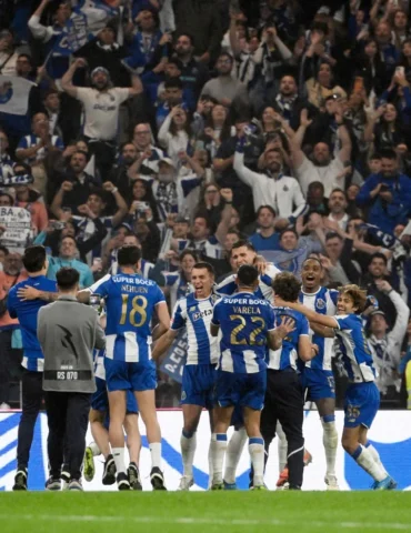 Soccer players in blue-and-white uniforms celebrate a goal on the field with cheering fans in the stands behind them