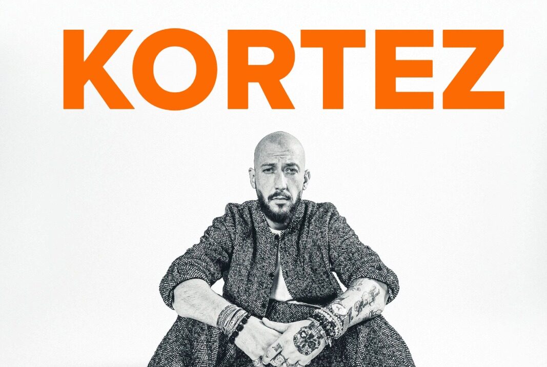 Poster for Kortesz tour: large orange 'KORTEZ' at top, a man seated in the center wearing a patterned suit and white sneakers; tour dates London and Manchester below.