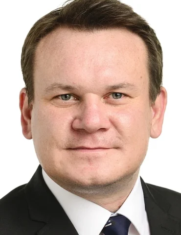 Head-and-shoulders portrait of a smiling man in a dark suit, white shirt, and navy tie.