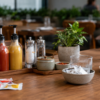 Condiment set on a wooden table with two squeeze bottles, salt and pepper grinders, spice bowls, and a potted plant in a restaurant. (informative)