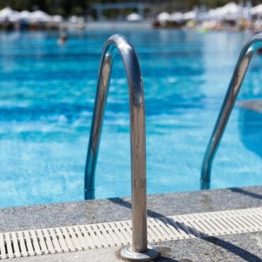 Stainless steel pool ladder rails at the edge of a bright blue outdoor swimming pool.