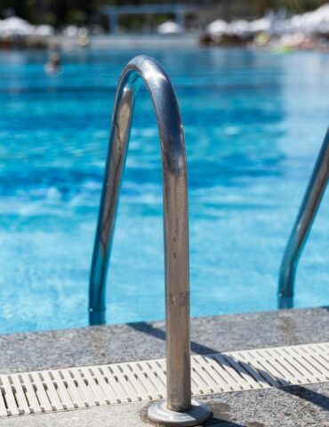 Stainless steel pool ladder rails at the edge of a bright blue outdoor swimming pool.