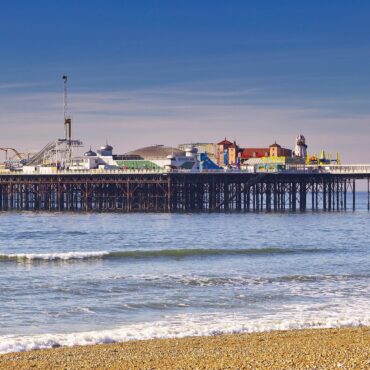 Pier with a colorful seaside amusement park on stilts over calm blue water under a clear sky.