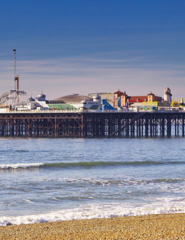 Pier with a colorful seaside amusement park on stilts over calm blue water under a clear sky.