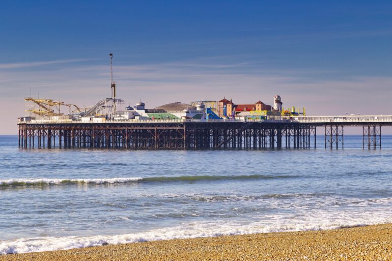 Pier with a colorful seaside amusement park on stilts over calm blue water under a clear sky.