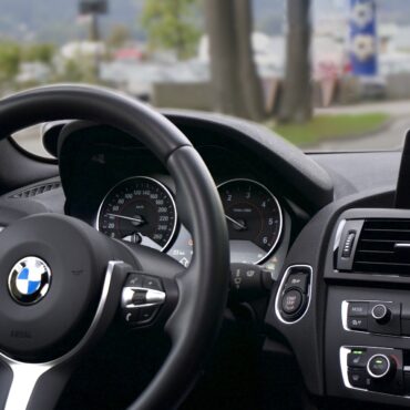 BMW car interior: steering wheel with logo, instrument cluster, and a navigation screen showing a map on the right side of the dashboard.
