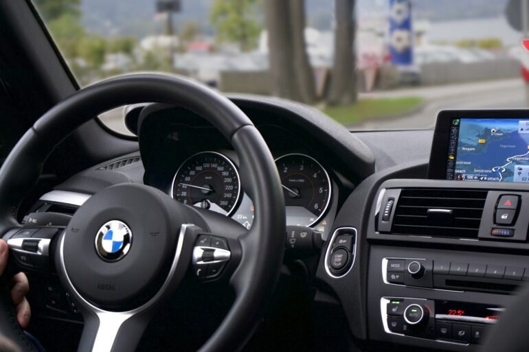 BMW car interior: steering wheel with logo, instrument cluster, and a navigation screen showing a map on the right side of the dashboard.