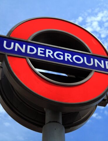 Close-up of a red London Underground roundel with a blue 'UNDEREGROUND' bar against a bright blue sky