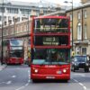 Red London double-decker bus in the foreground on a busy street, route 2 to Victoria Brixton Norwood Garage, with pedestrians nearby.
