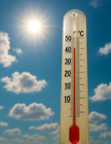 Outdoor thermometer with red mercury around 40°C against a bright, clear blue sky with sunshine.
