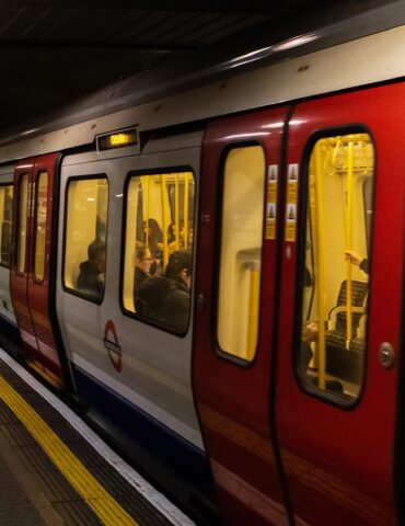 Subway train at an underground station, doors open, passengers inside and people waiting on the platform edge.