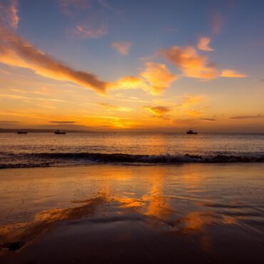 Sunset over calm sea with an orange sky and several boats near the horizon on the water.