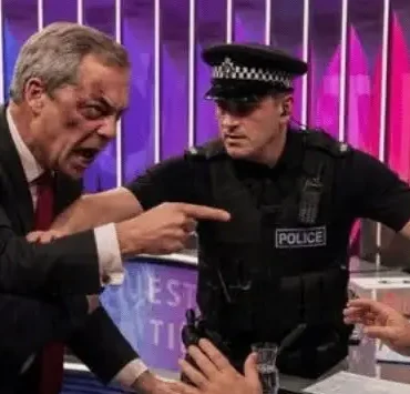 Politician yells at a man seated at a desk as two police officers separate them on a TV set.
