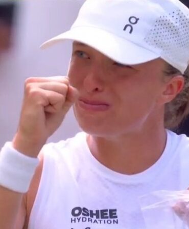 Female tennis player wearing a white cap wipes sweat from her face with a towel at the court.