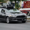 Autonomous Uber vehicle with a roof-mounted sensor rig driving on a city street, with a San Francisco Fire Department ambulance in the background.