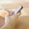 Person holding a smartphone in bed, screen blank, close-up on hands and device against peach-colored blanket