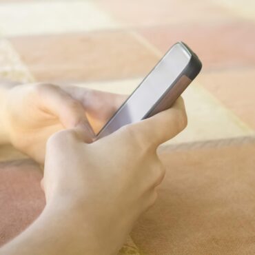 Person holding a smartphone in bed, screen blank, close-up on hands and device against peach-colored blanket