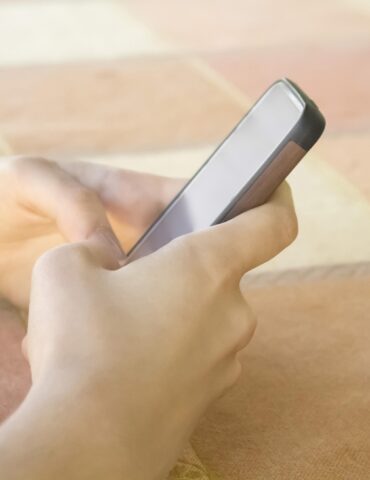 Person holding a smartphone in bed, screen blank, close-up on hands and device against peach-colored blanket
