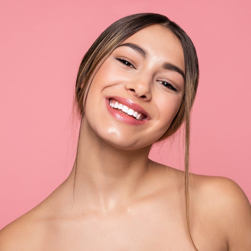 Smiling woman with light skin and brown hair in a loose updo against a pink background.