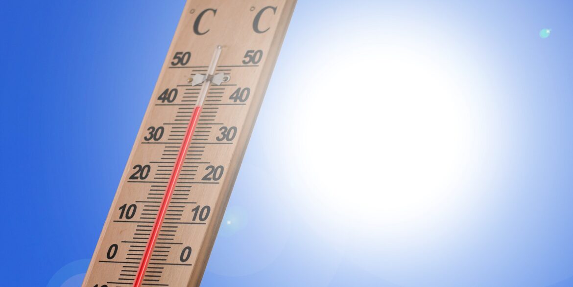 Wooden outdoor thermometer leaning against a bright blue sky with the sun, showing temperatures up to 50 (both scales visible).