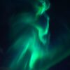 Aurora borealis (green northern lights) sweeping across a dark starry night sky.