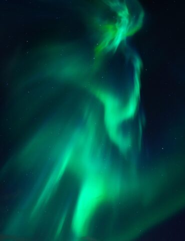 Aurora borealis (green northern lights) sweeping across a dark starry night sky.