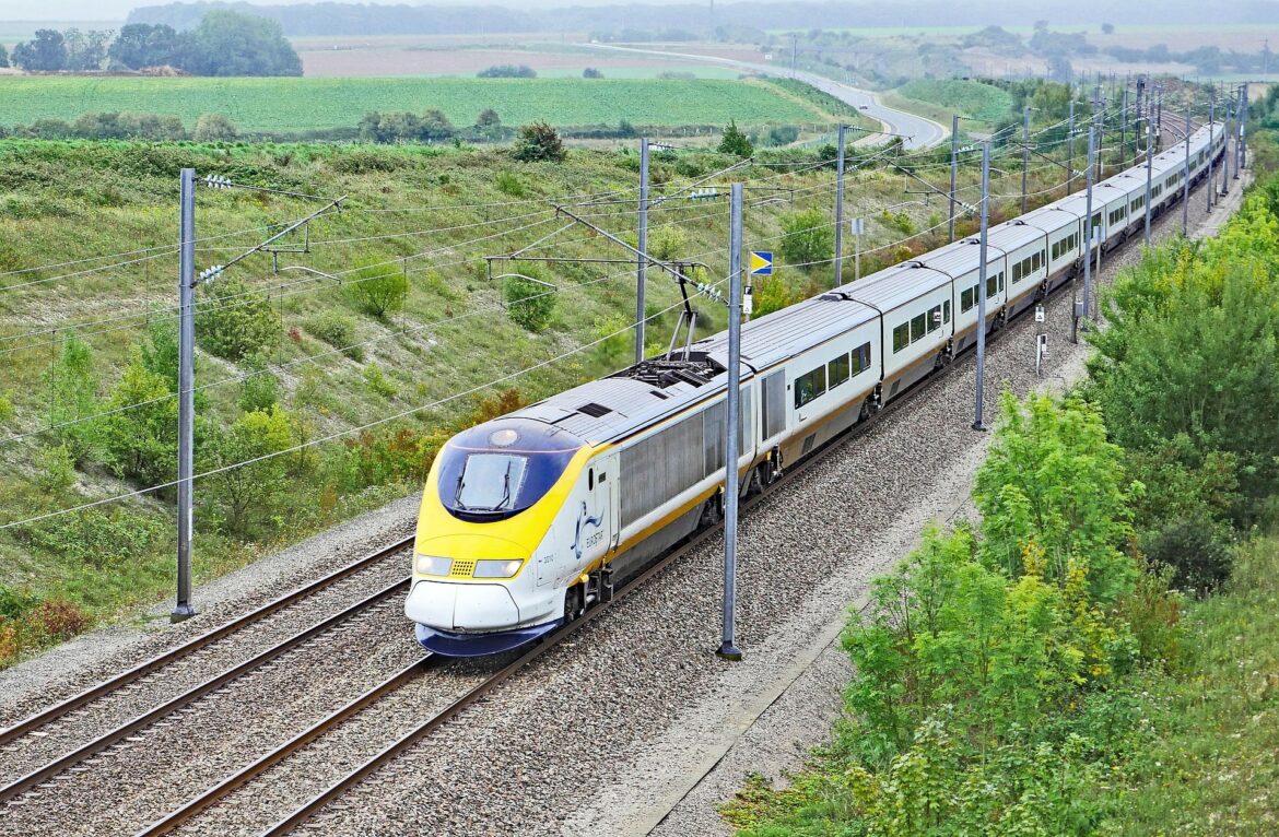 High-speed electric passenger train on elevated tracks through green countryside with overhead wires visible in the landscape