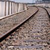 Railroad tracks curve to the right beside a gravel bed and a long white plastic fence on the left.