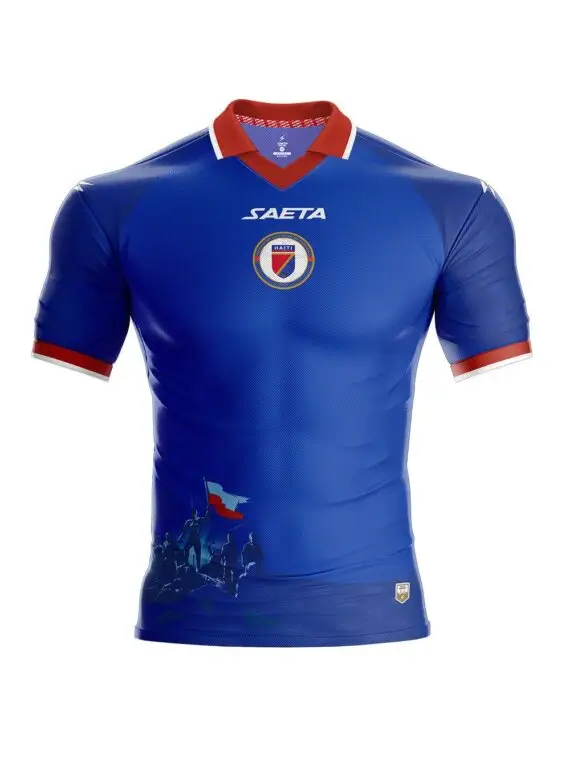 Blue Haiti national football jersey with red collar and white trim, features crest and SAETA logo on chest and stylized silhouettes at bottom left