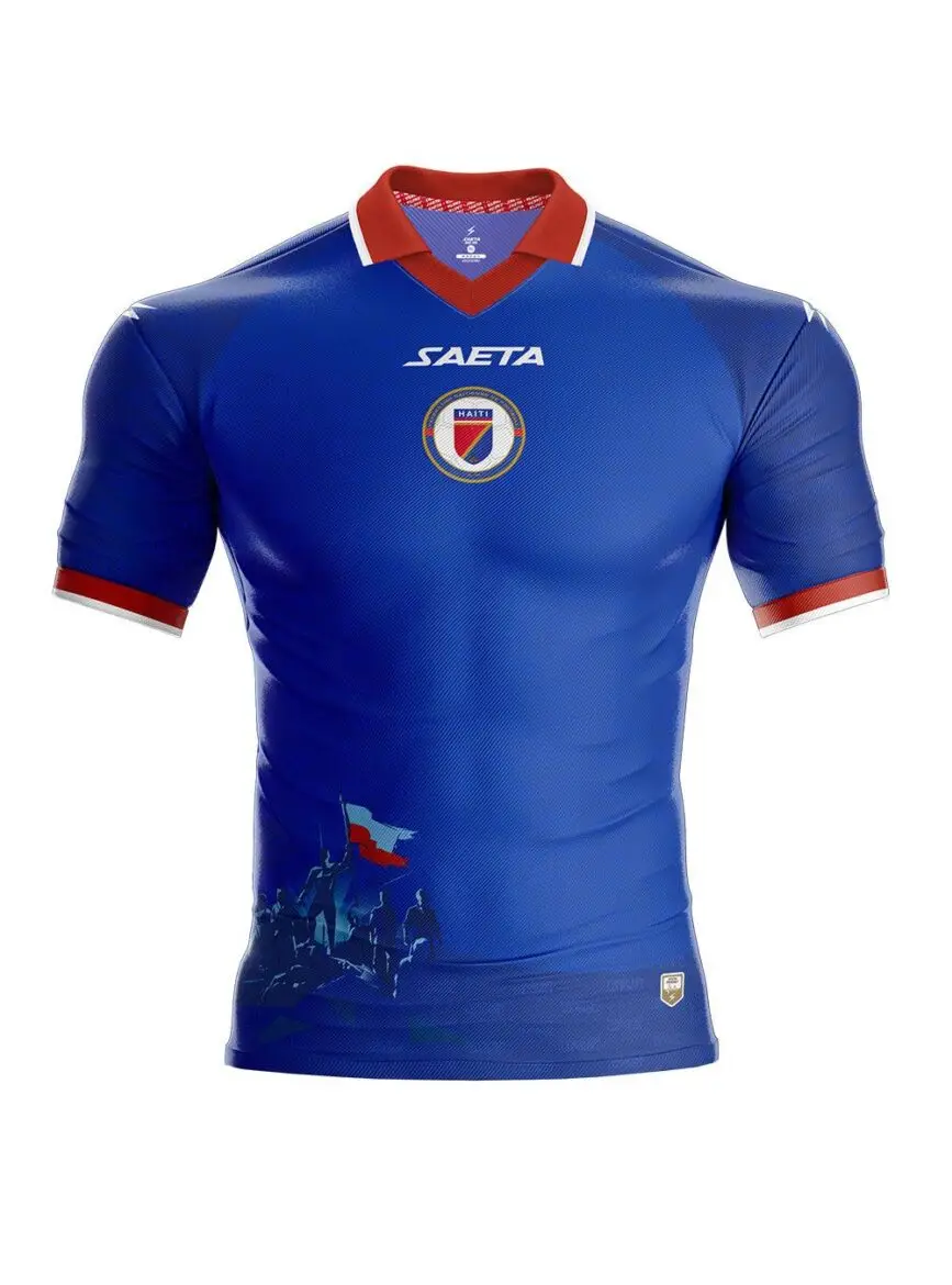 Blue Haiti national football jersey with red collar and white trim, features crest and SAETA logo on chest and stylized silhouettes at bottom left
