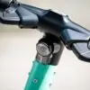 Close-up of a black bicycle handlebar stem with a circular front light mounted on the teal frame area beneath.