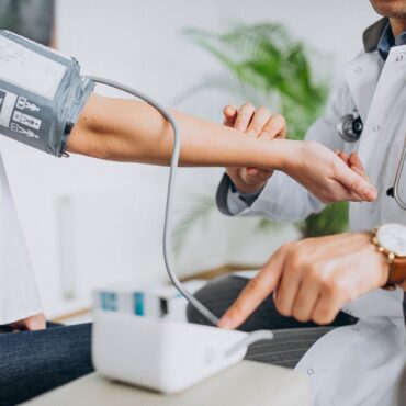 Doctor checks patient’s blood pressure using a cuff; a stethoscope rests around the doctor’s neck.