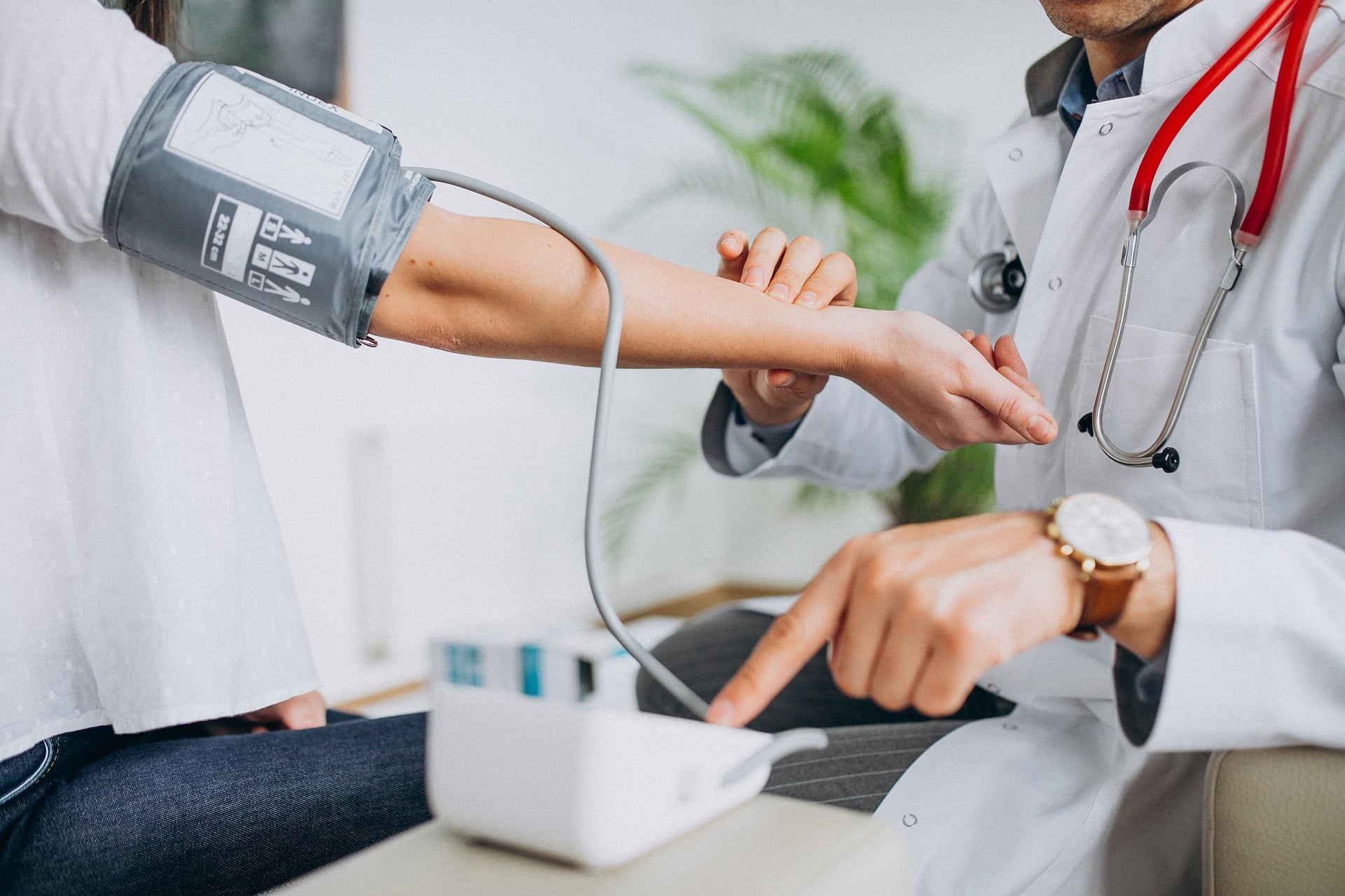 Doctor checks patient’s blood pressure using a cuff; a stethoscope rests around the doctor’s neck.