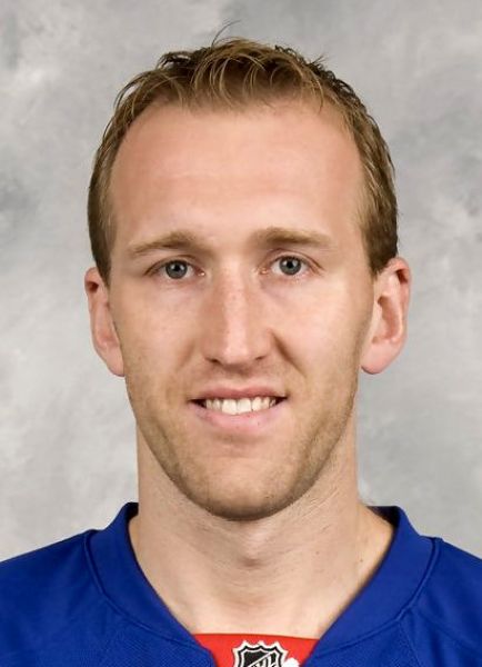 Head-and-shoulders portrait of a man in a blue hockey jersey, facing the camera with a slight smile.